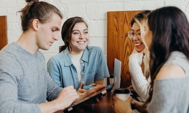 Eine Gruppe von Menschen stehen an einem Tisch, eine Person hat ein Tablet in der Hand