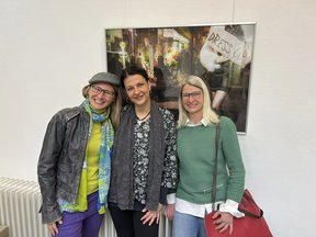 Drei Personen vor einem Foto an der Wand