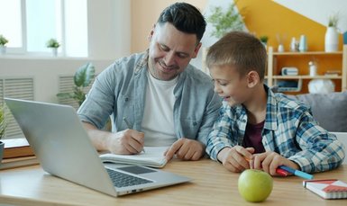 Vater mit kleinem Kind vor einem Laptop zeichnet etwas, ein Apfel liegt davor