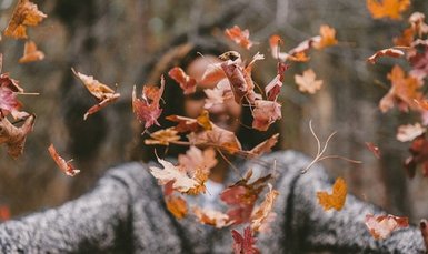 Mensch wirft Herbstlaub hoch