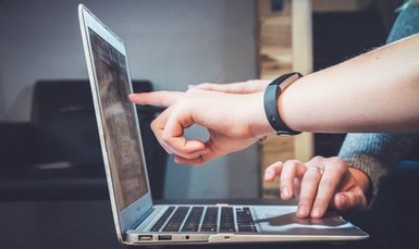 Eine Hand liegt auf der Tastatur eines Laptops, eine weitere Hand einer anderen Person zeigt auf den Bildschirm des gleichen Laptops