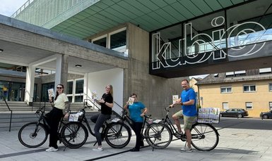 Drei Personen jeweils mit einem Fahrrad halten das neue vhs Programmheft hoch